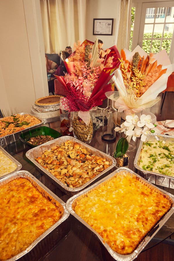 Aluminum dishes filled with food sit on a table next to serving dishes, a pie and two flower arrangements.